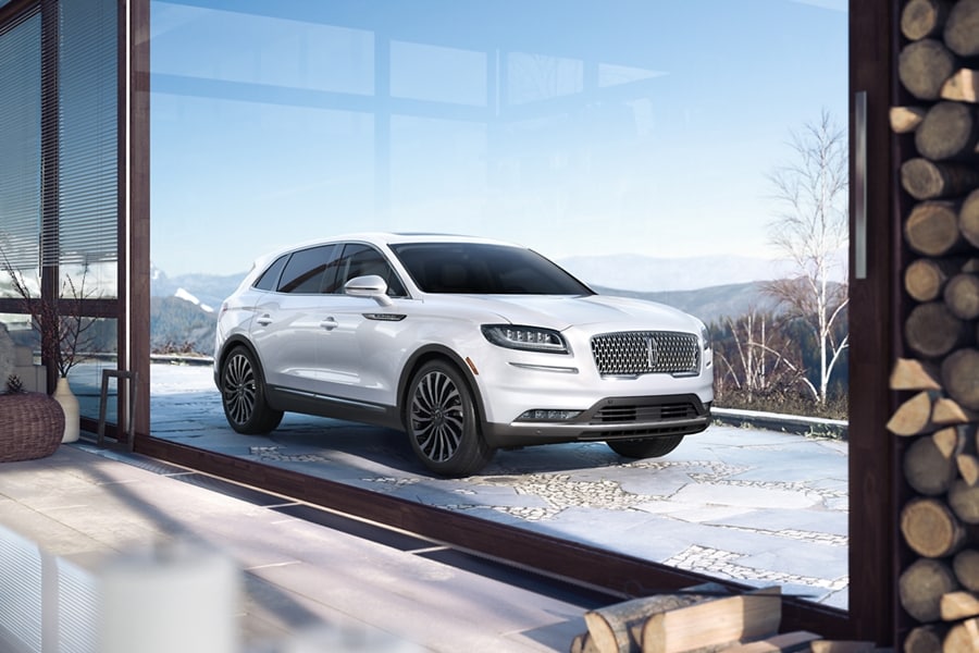 Se muestra una SUV Lincoln Black Label Nautilus® 2023 con el tema Chalet estacionada en la entrada de una lujosa casa de montaña