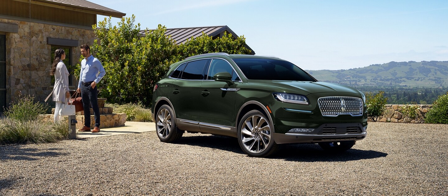 A couple is standing outside a cobblestone home next to a 2023 Lincoln Nautilus® SUV