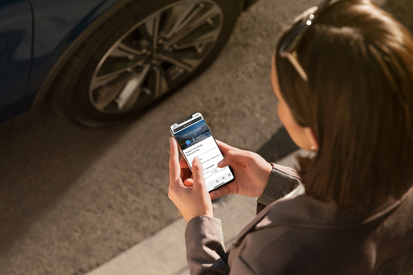 Una mujer interactúa con la aplicación Calm en su smartphone mientras se acerca a su vehículo Lincoln.