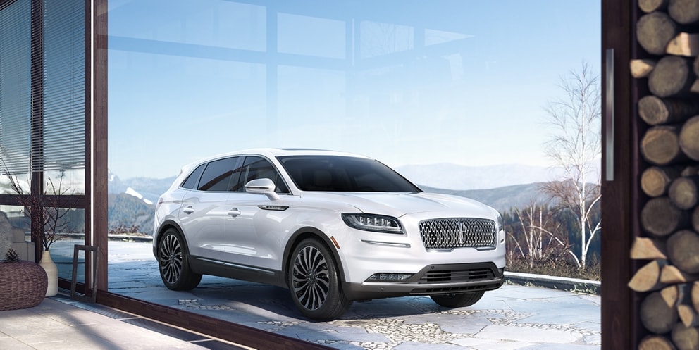 Se muestra una SUV Lincoln Black Label Nautilus® 2023 con el tema Chalet estacionada en la entrada de una lujosa casa de montaña