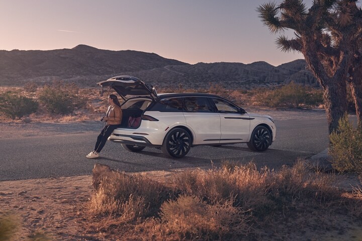 A person is shown sitting on the rear bumper of a 2025 Lincoln Black Label Nautilus® SUV with the rear liftgate open