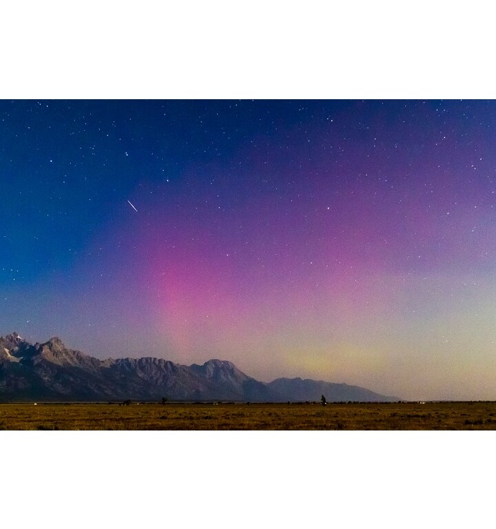 A comet streaks across a night sky that is brightened by the northern lights