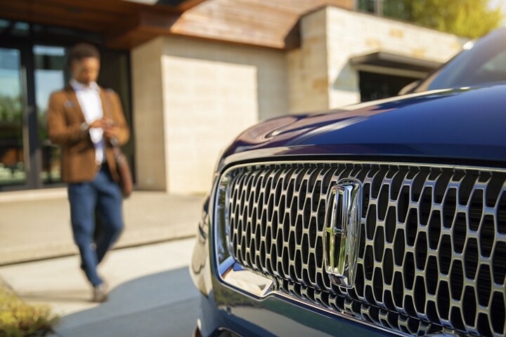 A person approaches a Lincoln vehicle while using a smartphone