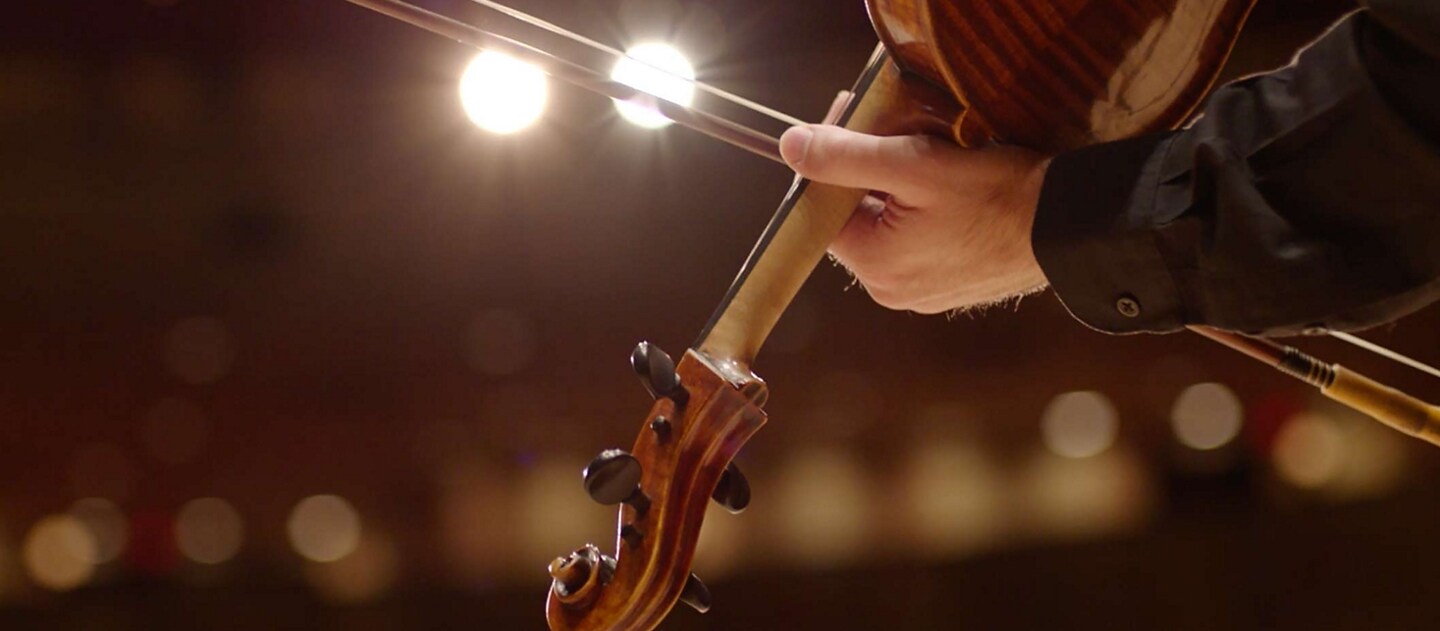 El arco del violín de un músico se desliza bajo las luces del escenario de manera de ilustrar el impresionante sonido de los tonos sinfónicos.