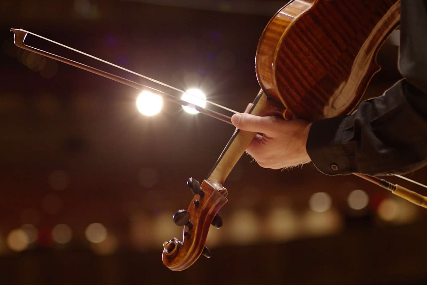 The bow of a musician’s violin slides across stage spotlights to illustrate the dramatic sound of the symphonic chimes.