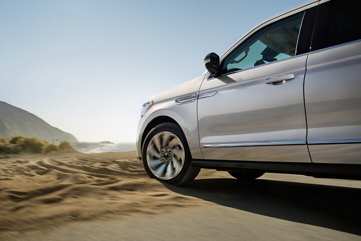 A 2023 Lincoln Navigator® SUV with available four-wheel drive is being driven in sandy terrain.