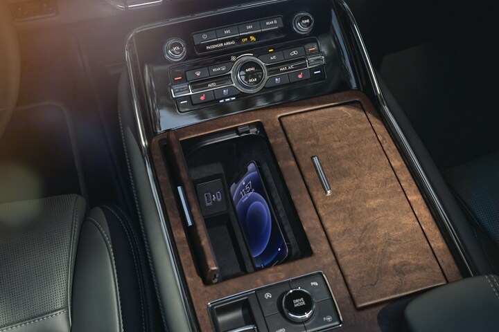 A smartphone is charging on the wireless charging pad that is tucked in a cubby integrated into the front center console.