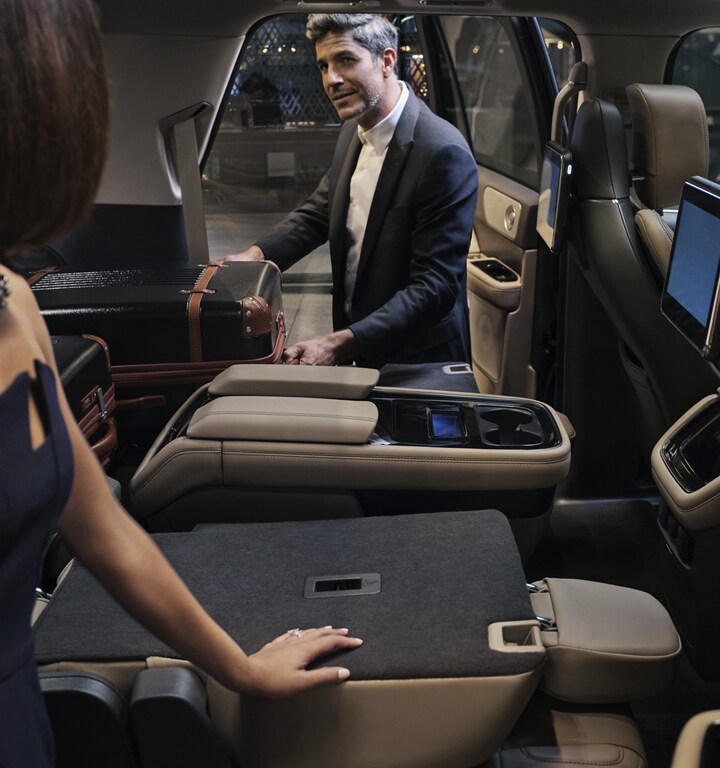 A man is pulling a suitcase out of the folded-flat second-row seat of a 2023 Lincoln Navigator® SUV.