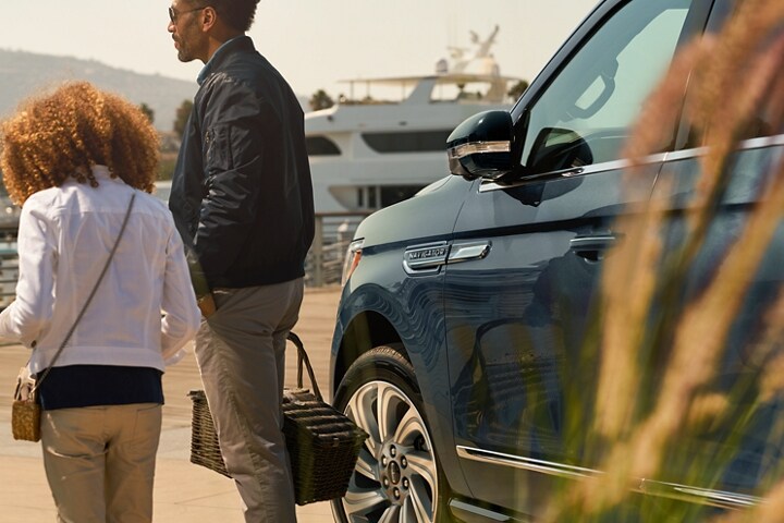 A little girl and dad walk away from a 2023 Lincoln Navigator® SUV with its sideview mirrors folded.