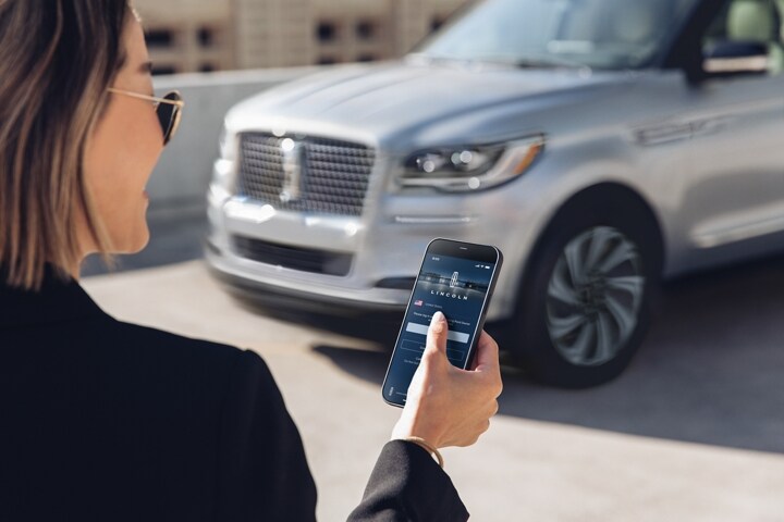 A woman is outside and interacts with the Lincoln Way App as she approaches her Lincoln.