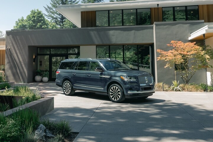 A 2023 Lincoln Navigator® SUV is parked in front of a beautiful mid-century modern home on a sunny day.