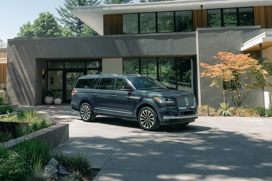 Una SUV Lincoln Navigator® 2023 está estacionada delante de una bonita casa moderna de mediados de siglo en un día soleado.