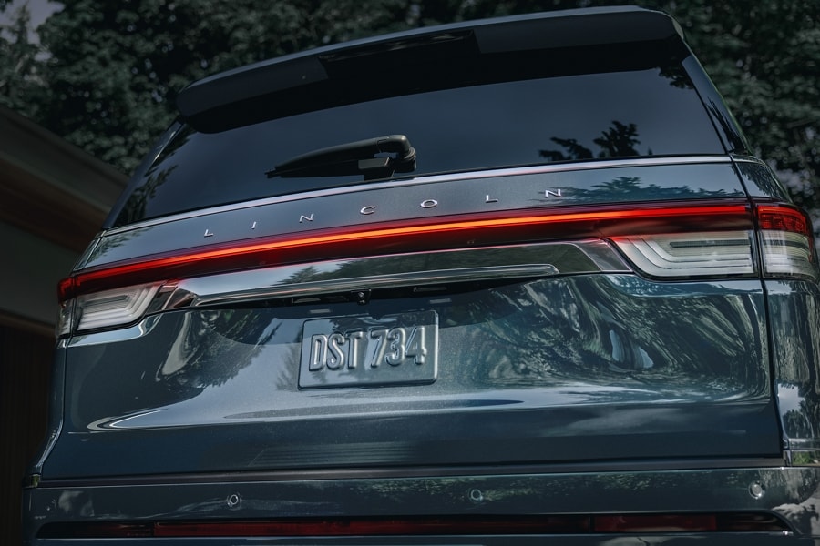 The rear design of a 2023 Lincoln Navigator® SUV shows off glowing taillamps illuminating with the Lincoln Embrace.