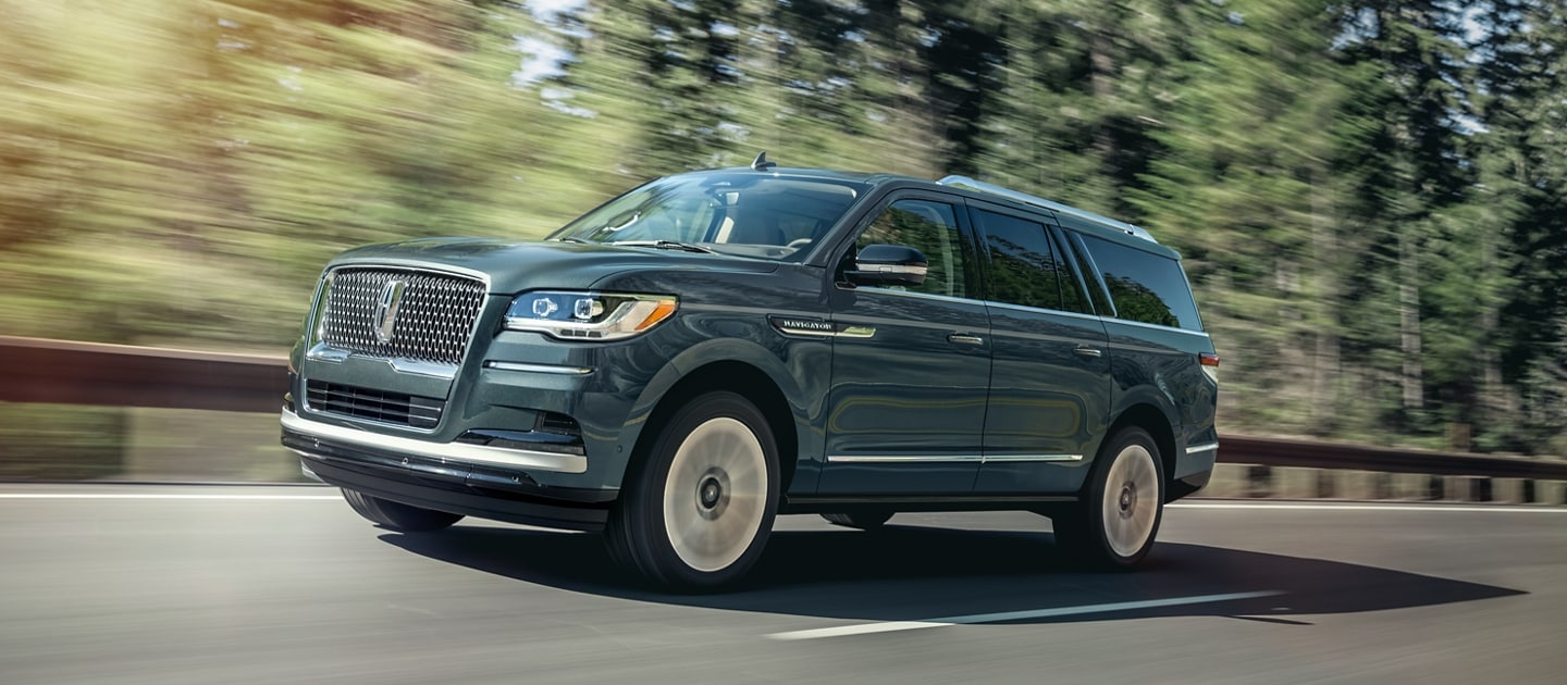 Una SUV Lincoln Navigator® 2023 circula por una carretera con pinos altos bajo la luz del sol.