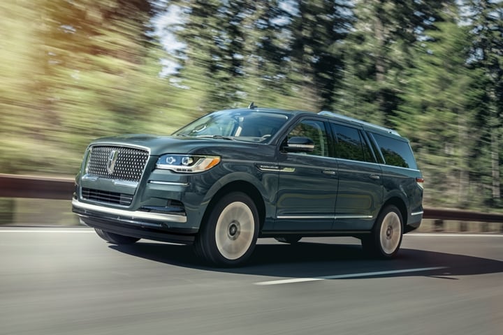 A 2023 Lincoln Navigator® SUV in Flight Blue is being driven up an incline surrounded by greenery.
