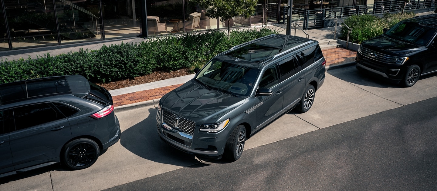 Una SUV Lincoln Navigator® 2023 estacionada en paralo entre dos autos en una calle del centro frente a un hotel de lujo.