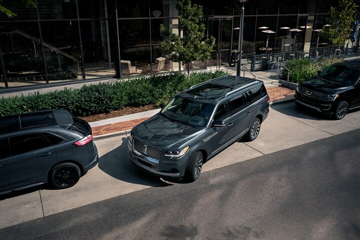 A 2023 Lincoln Navigator® SUV is being parked on the side of a downtown street in between two other vehicles.