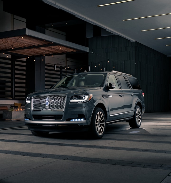 A man and woman in formal wear are approaching a 2023 Lincoln Navigator® SUV at night as it lights with the Lincoln Embrace.