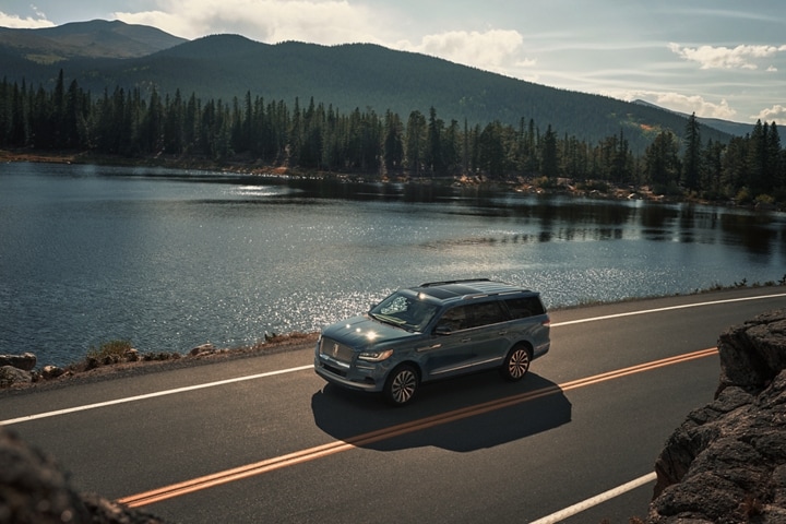 A 2023 Lincoln Navigator® SUV is being driven along a lake in the mountains.