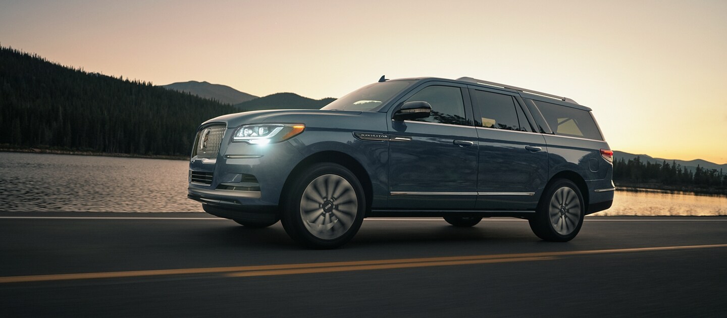 Una SUV Lincoln Navigator® 2023 circulando en la montaña mientras el sol del atardecer se refleja en el agua.