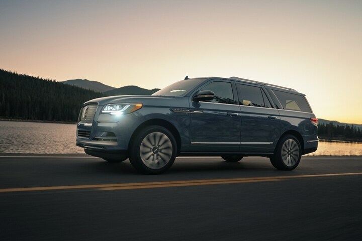 A 2023 Lincoln Navigator® SUV is being driven in the mountains at sunset as light bounces off the calm waters.