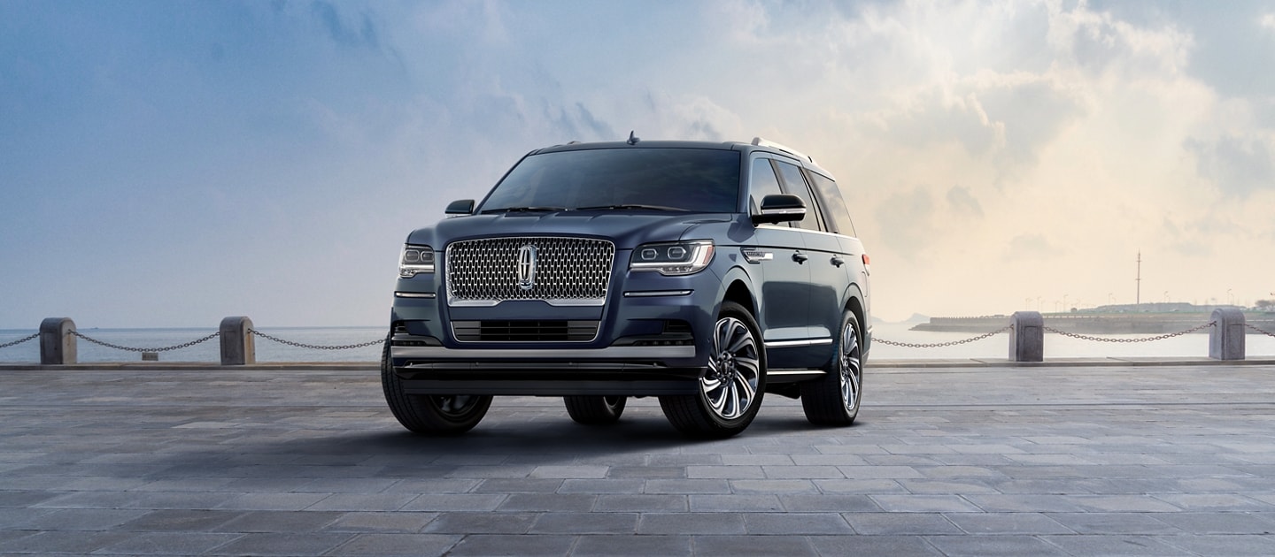 Un modelo de la SUV ​​​​​​​Lincoln Navigator® Reserve 2023​​​​​​​ en azul océano profundo estacionado cerca de una bahía bajo un cielo con nubes.