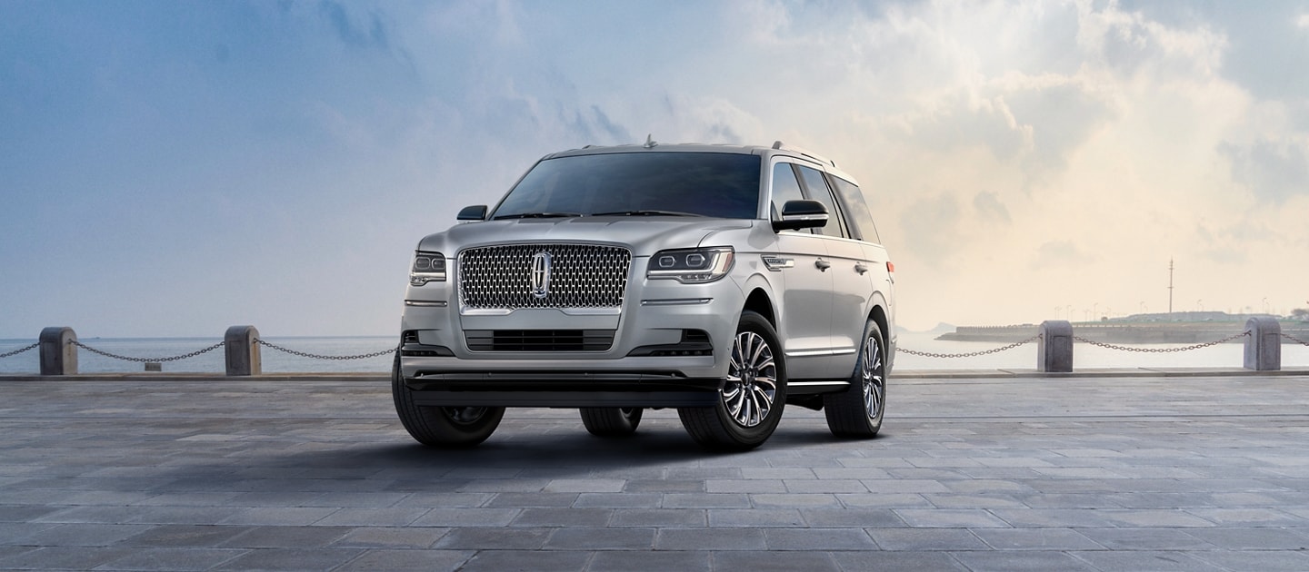 A 2023 Lincoln Navigator® SUV in Silver Radiance is parked near a bay beneath a cloudy sky.