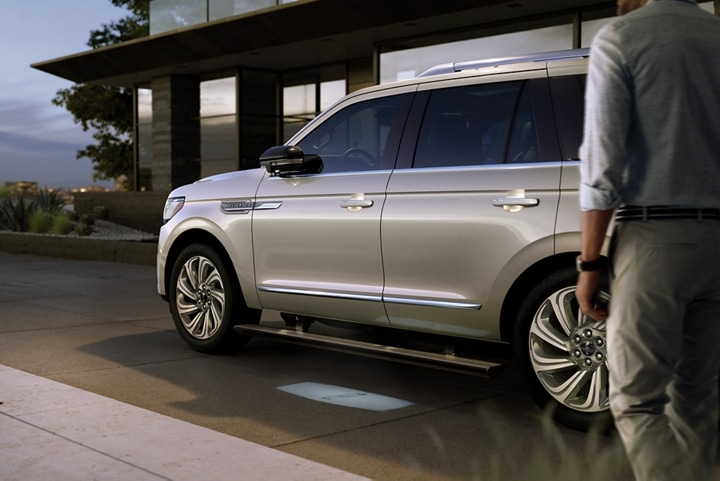 A 2024 Lincoln Navigator® SUV with extended running boards is parked in front of a modern home