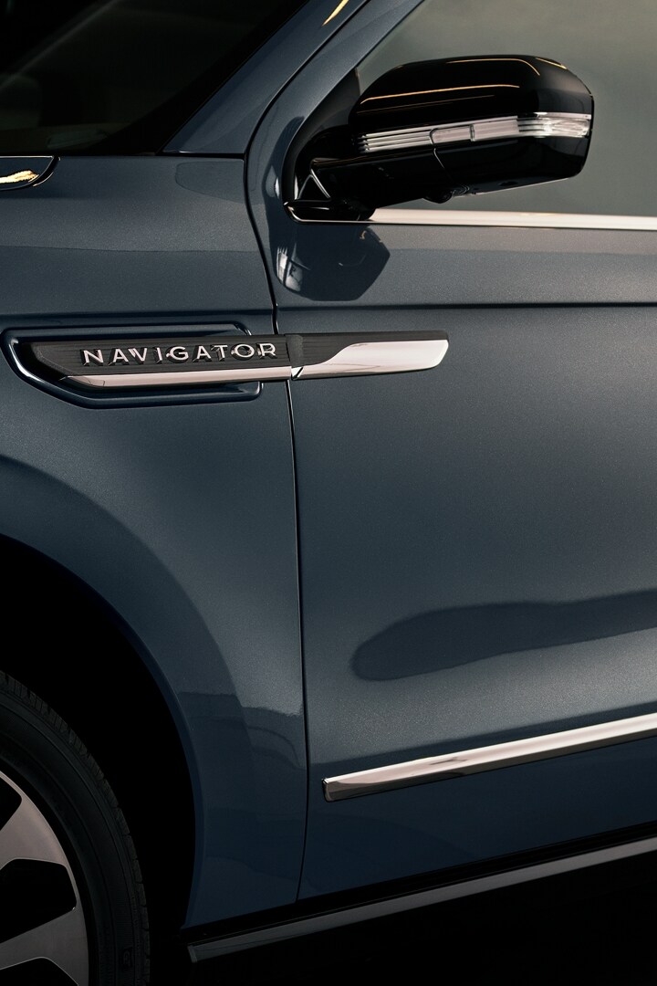 A woman is approaching a 2024 Lincoln Navigator® SUV with an elegant clear purse displaying a smartphone and lipstick