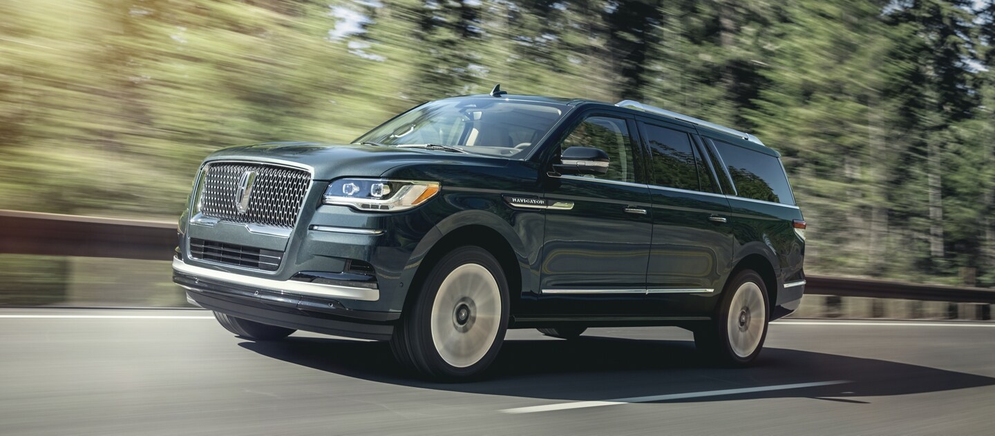 Una SUV Lincoln Navigator® 2024 circula por una carretera con pinos altos bajo la luz del sol.