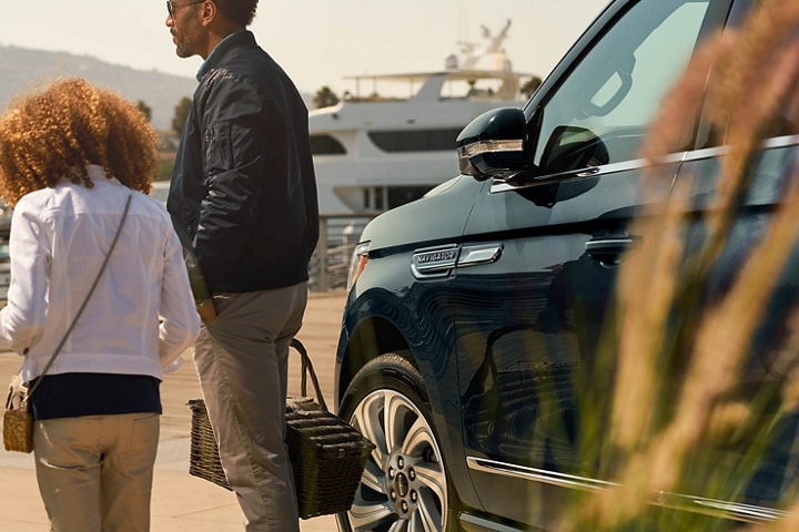 Una niña pequeña y su papá se alejan de una SUV Lincoln Navigator® 2024 con los espejos laterales plegados.