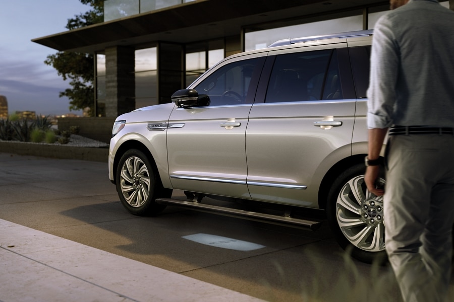 A 2024 Lincoln Navigator® SUV with extended running boards is parked in front of a modern home.
