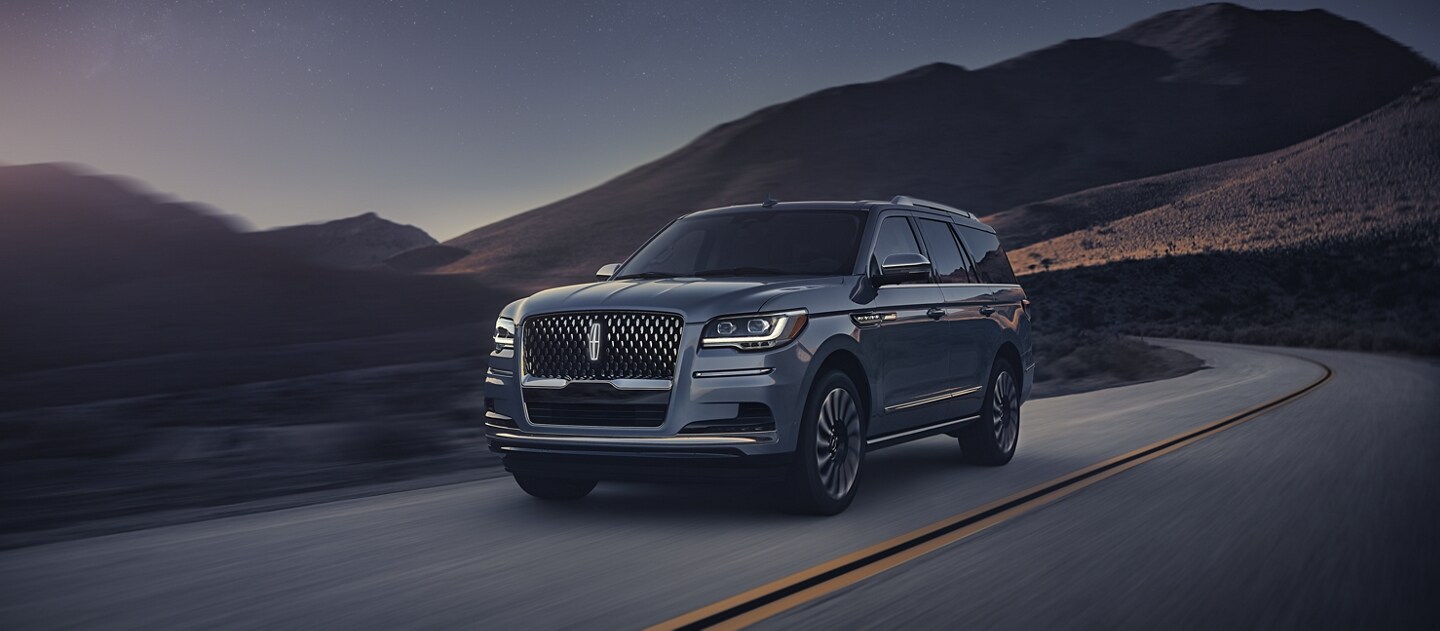 A 2024 Lincoln Navigator® SUV is being driven along a curved road in the mountains.