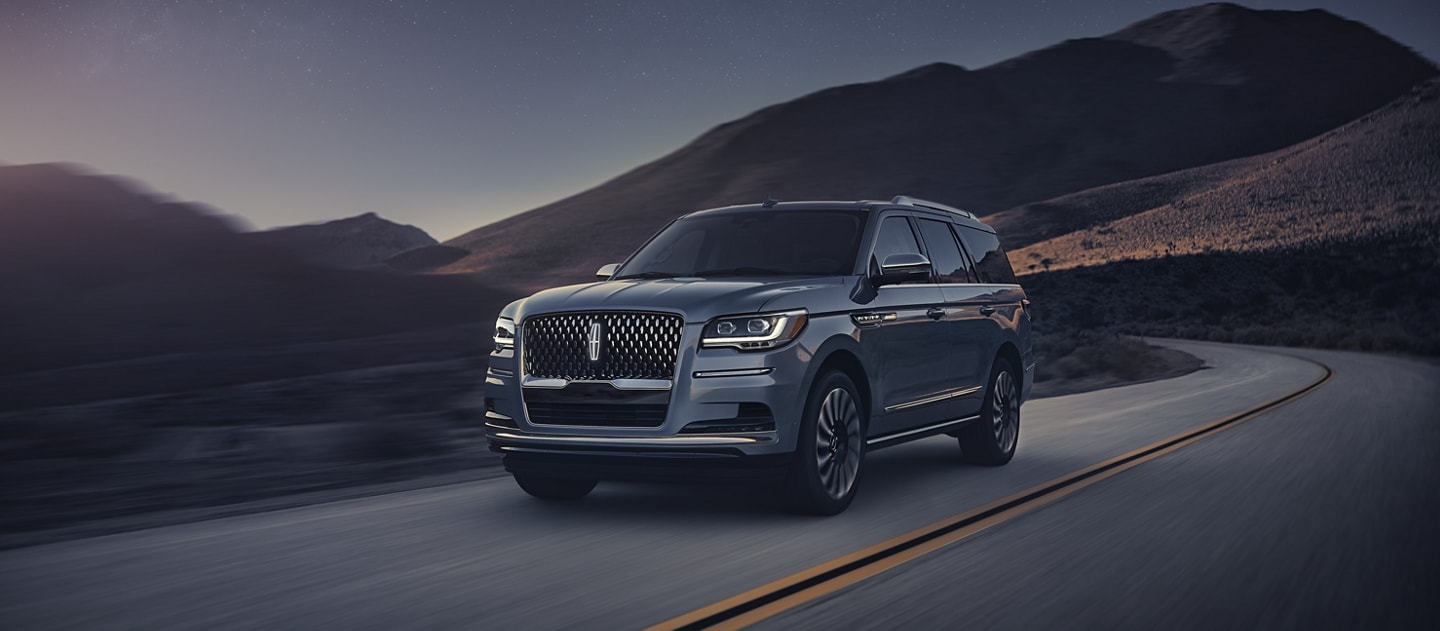 A 2024 Lincoln Navigator® SUV is being driven along a curved road in the mountains.