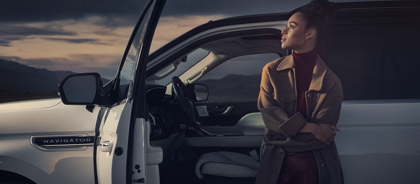 Una mujer parada al lado de una SUV Lincoln Black Label Navigator® 2024 con la puerta abierta que muestra el interior con el tema Chalet.