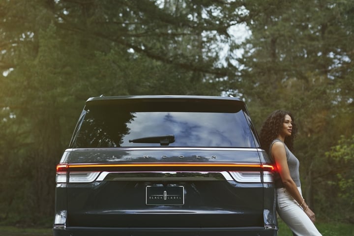 Una mujer se relaja contra el costado de una SUV Lincoln Black Label Navigator® 2024.