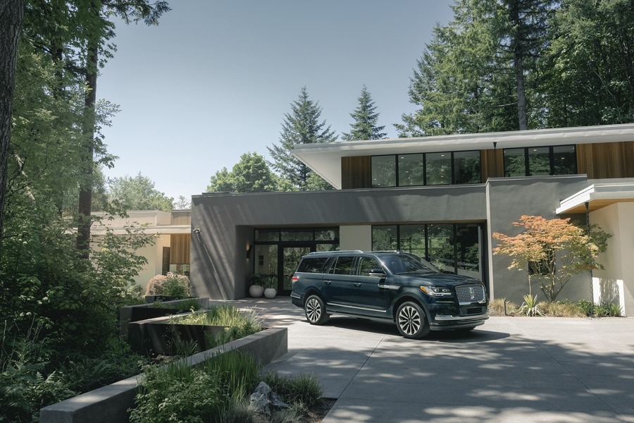 Una SUV Lincoln Navigator® 2024 está estacionada delante de una bonita casa moderna de mediados de siglo en un día soleado.