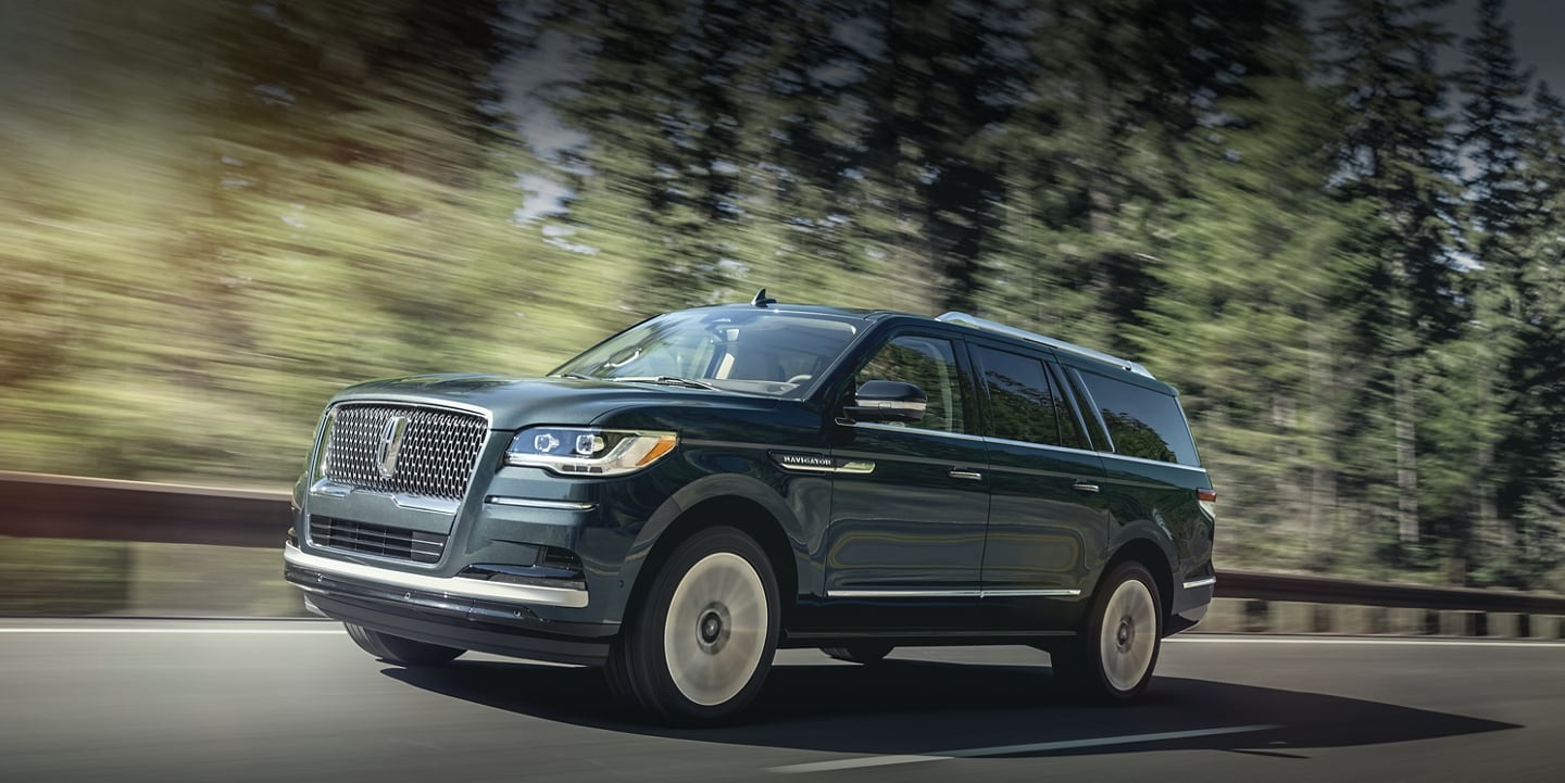 A 2024 Lincoln Navigator® SUV in Flight Blue is being driven up an incline surrounded by greenery.