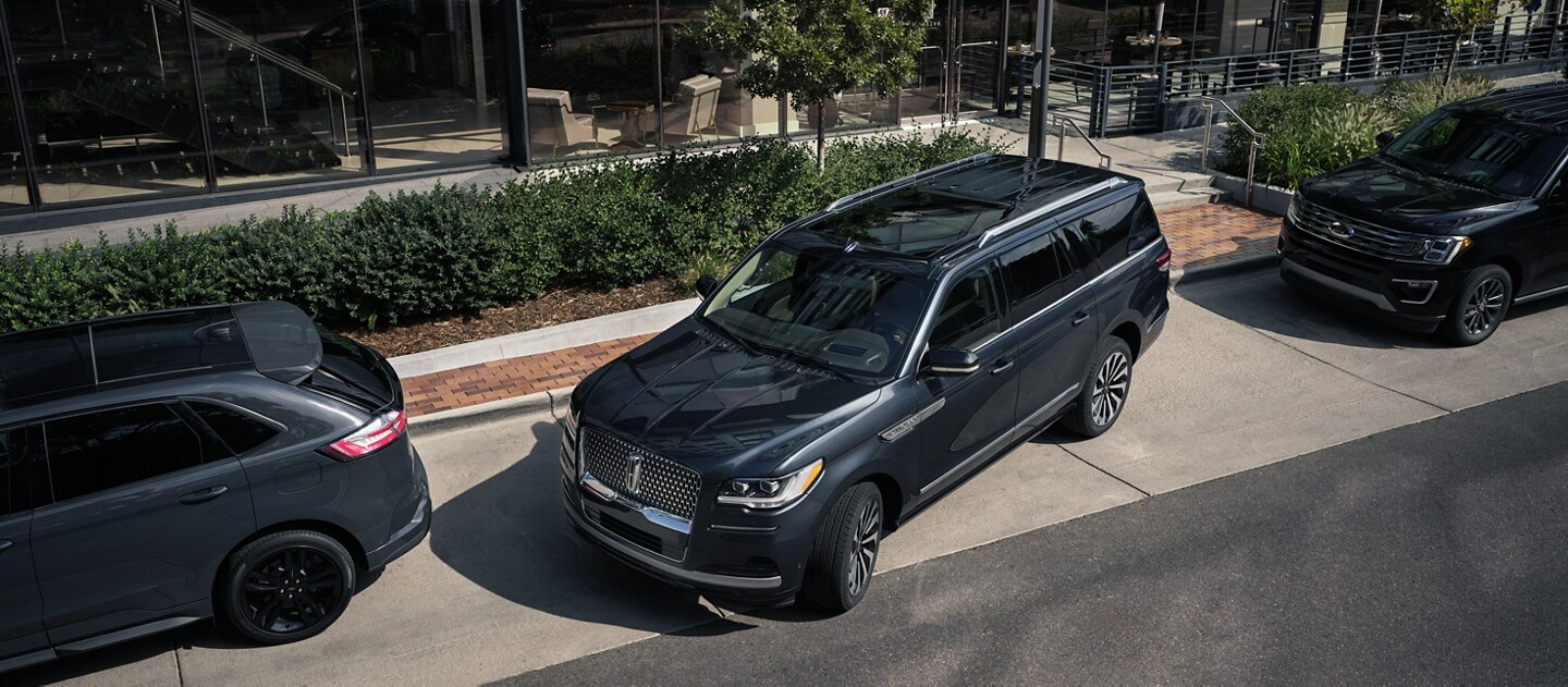 Una SUV Lincoln Navigator® 2024 estacionada en paralo entre dos autos en una calle del centro frente a un hotel de lujo.