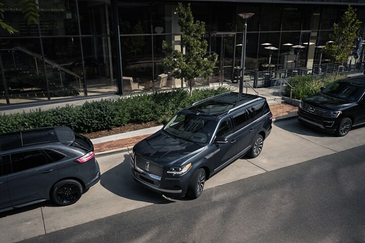 A 2024 Lincoln Navigator® SUV is being parked on the side of a downtown street in between two other vehicles.