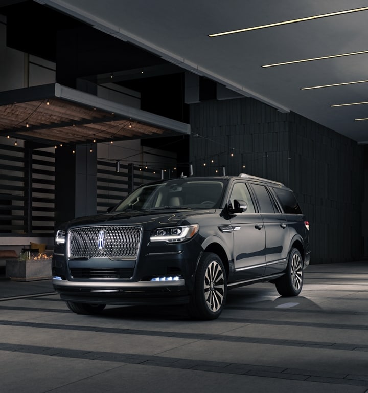 A man and woman in formal wear are approaching a 2024 Lincoln Navigator® SUV at night as it lights with the Lincoln Embrace.