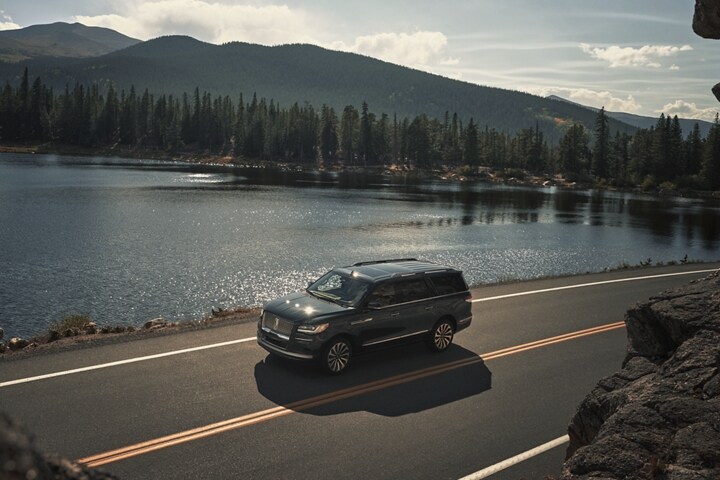 A 2024 Lincoln Navigator® SUV is being driven along a lake in the mountains.