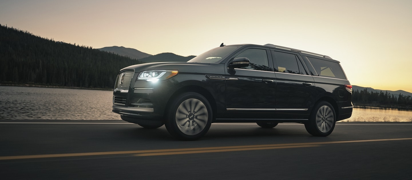 A 2024 Lincoln Navigator® SUV is being driven in the mountains while the setting sun washes over the reflective water.
