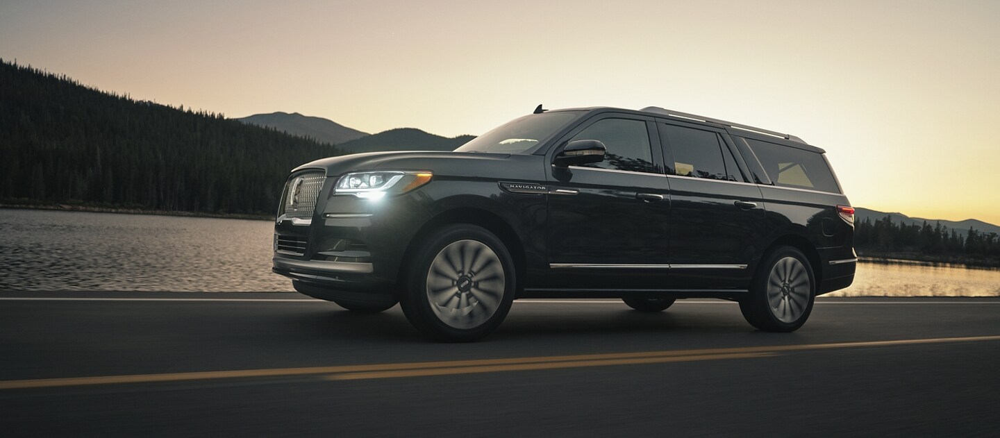 Una SUV Lincoln Navigator® 2024 circulando en la montaña mientras el sol del atardecer se refleja en el agua.