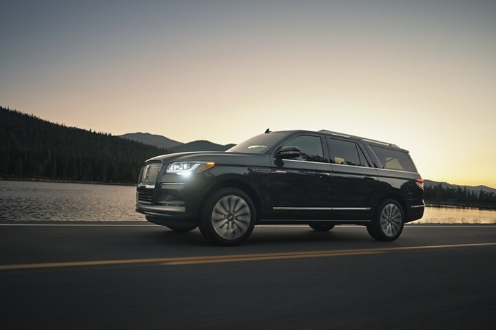 A 2024 Lincoln Navigator® SUV is being driven in the mountains at sunset as light bounces off the calm waters.