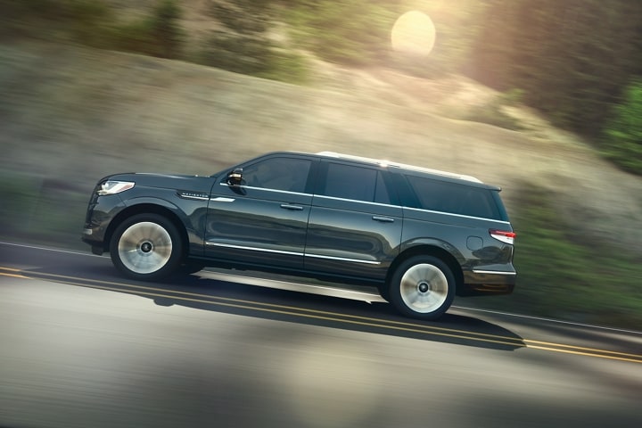 A 2024 Lincoln Navigator® SUV in Flight Blue is being driven up an incline surrounded by greenery.