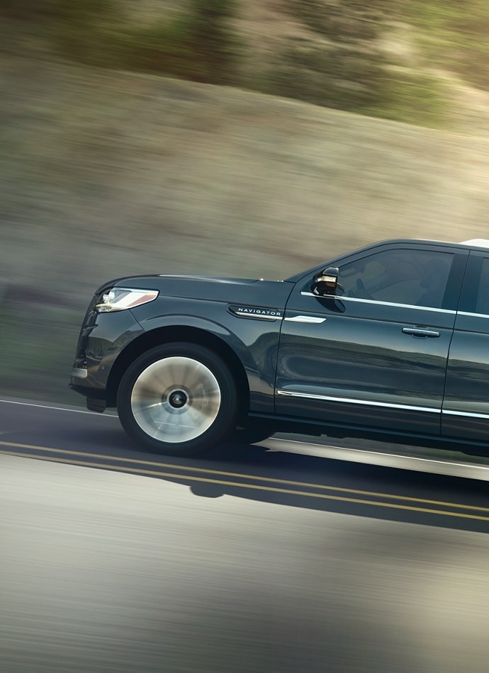 A 2024 Lincoln Navigator® SUV in Flight Blue is being driven up an incline surrounded by greenery