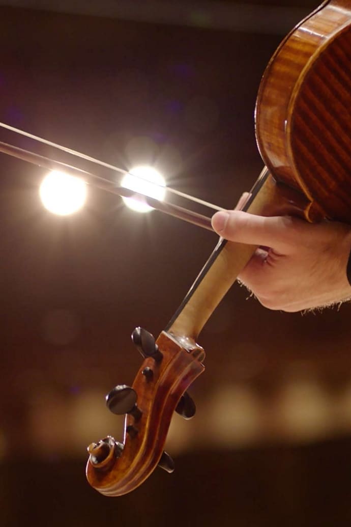 The bow of a musician’s violin slides across stage spotlights to illustrate the dramatic sound of the symphonic chimes