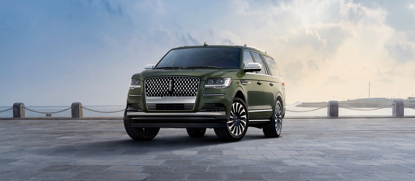 Un modelo SUV Lincoln Black Label Navigator® L 2024 en verde Manhattan estacionado en una pintoresca bahía bajo un hermoso cielo pintado con acuarelas.