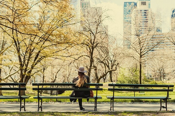 Una persona llevando un sombrero flexible sentado en un banco en Central Park contemplando el paisaje.